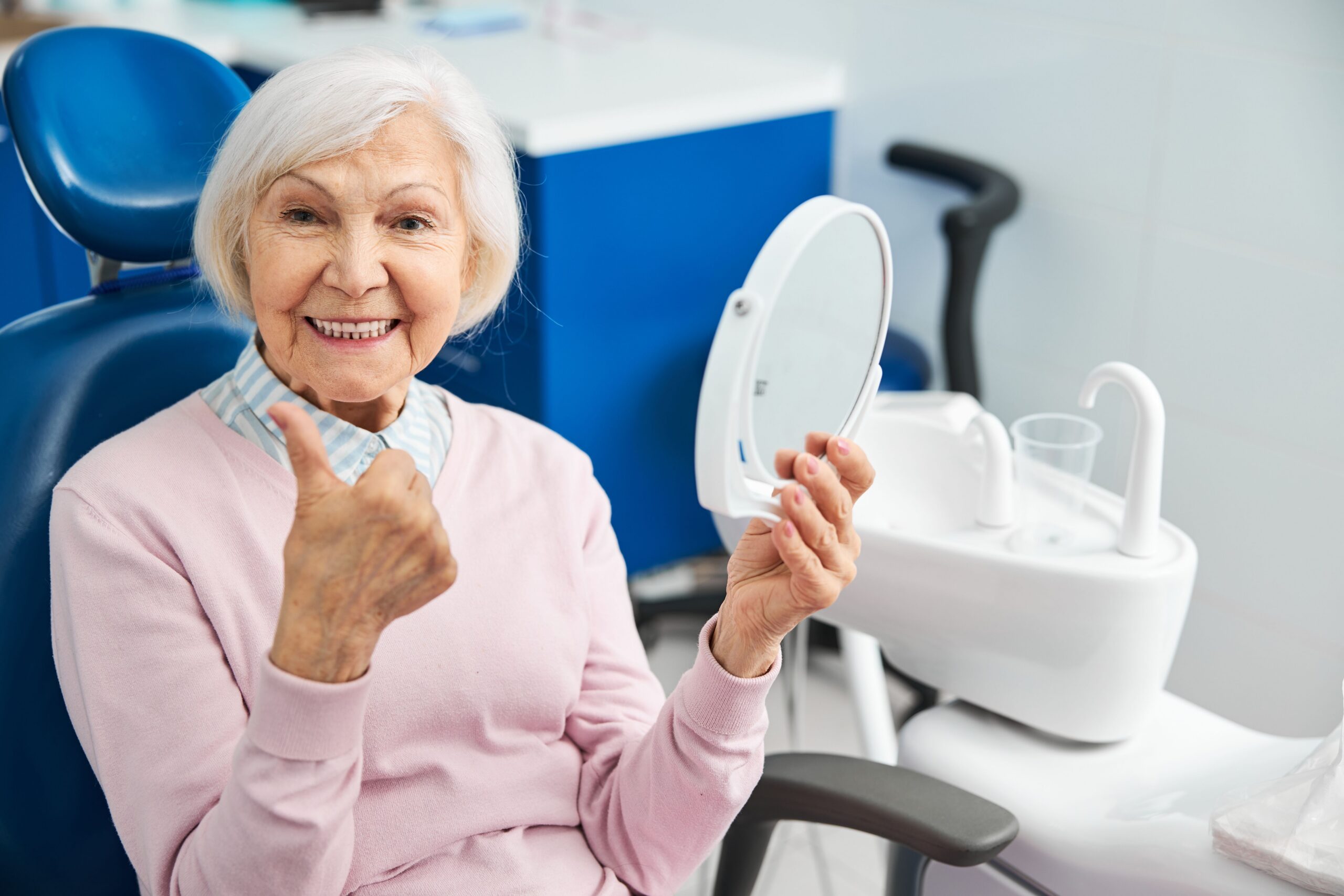 Elderly woman in the dental chair admiring her new smile in a mirror.