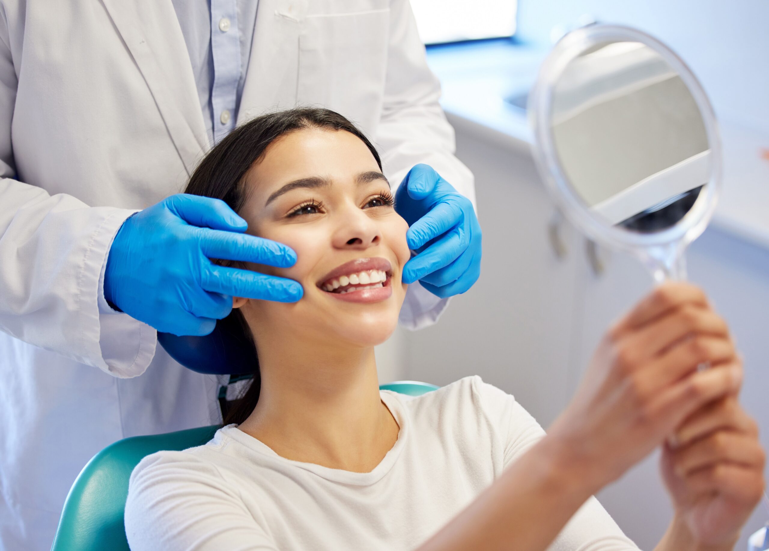 Woman admiring her smile in a handheld mirror after cosmetic dental treatment.