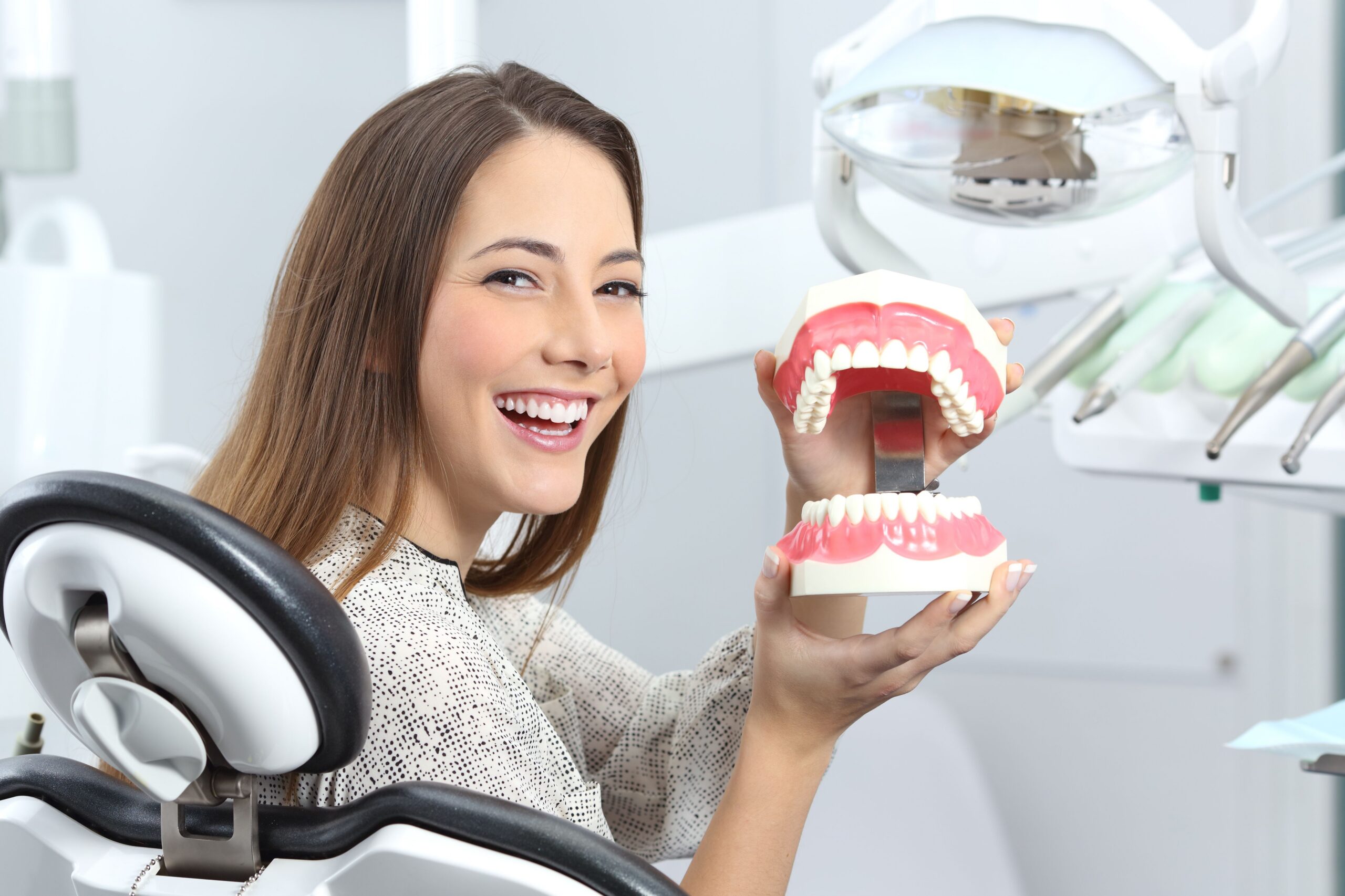 Woman in the dental chair holding a model of her teeth during a denture fitting.