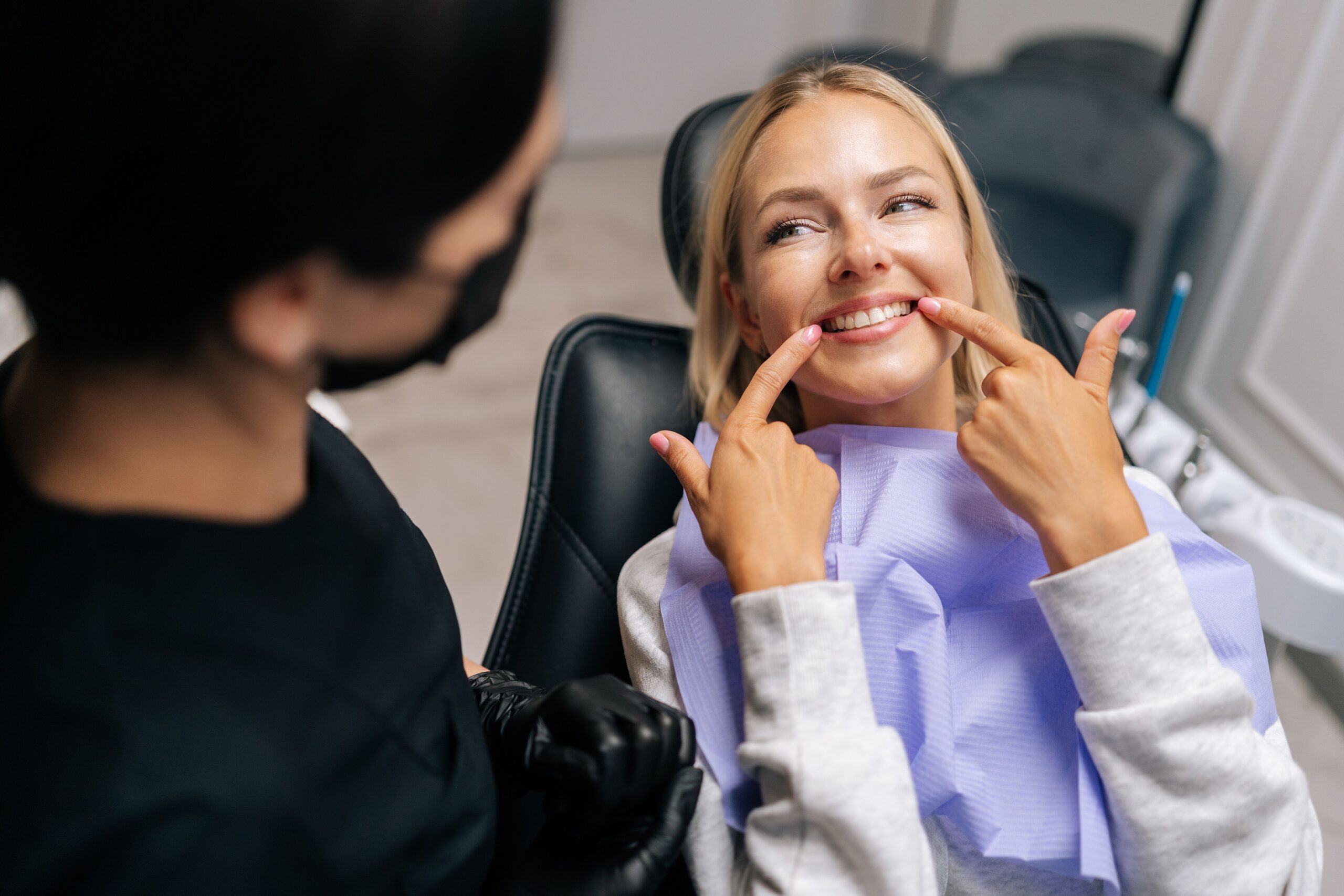 Woman sitting in the dental chair pointing to her teeth during a clear aligner consultation.